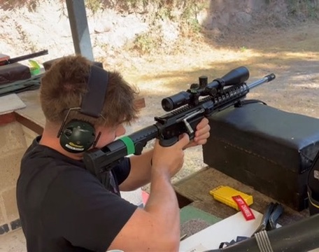 Member aiming a scoped rifle from a shooting bench — enlarge photo